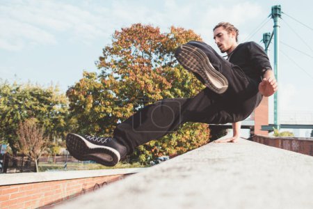 Photo for Acrobatic young man outdoors training parkour tricks exercises free running - Royalty Free Image