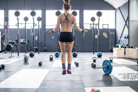 Foto de Back view young athletic woman indoor gym jumping rope - fitness, training, sportive concept - Imagen libre de derechos