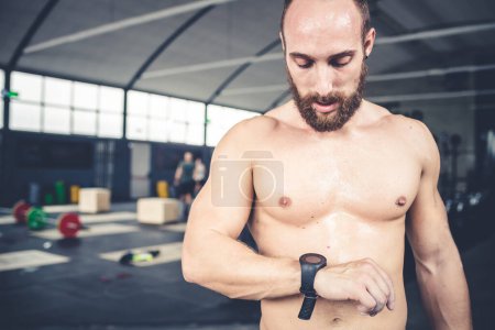Foto de Athletic young man using smart watch and smartphone indoors gym after training - technology, sportive, fitness concept - Imagen libre de derechos