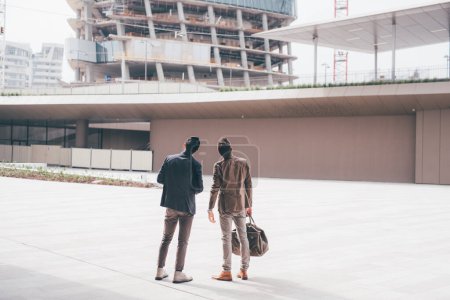 Foto de Dos jóvenes empresarios contemporáneos miran hacia atrás al aire libre ciudad buscando paisaje urbano, contemplativos y reflexivos compañeros de trabajo - Imagen libre de derechos
