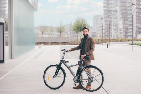 Téléchargez les photos : Jeune homme barbu contemporain faisant du vélo en ville à l'extérieur et se déplaçant sans carbone - en image libre de droit