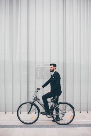 Elegant executive bearded young professional businessman going to work by bike commuting the carbon-free way