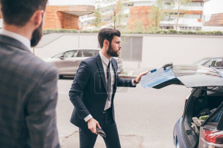 Photo for Contemporary elegant bearded businessman outdoors closing car trunk - Royalty Free Image