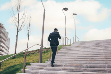 Téléchargez les photos : Jeune homme d'affaires en plein air monter les escaliers parler smartphone, ambition pour l'avenir - en image libre de droit