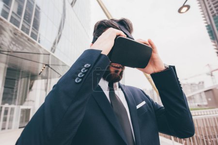 Foto de Elegante ejecutivo profesional hombre de negocios barbudo utilizando visor 3D al aire libre explorar el ciberespacio metaverso - Imagen libre de derechos