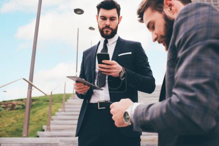 Téléchargez les photos : Deux jeunes hommes d'affaires élégants en plein air partageant et utilisant une tablette informatique - en image libre de droit