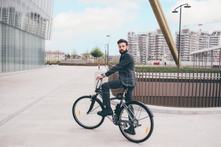 Foto de Elegante barbudo joven y elegante hombre de negocios que va a trabajar en bicicleta conmutando el camino libre de carbono - Imagen libre de derechos