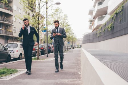 Téléchargez les photos : Deux hommes d'affaires à l'extérieur en utilisant tablette et smartphone discuter et planifier le travail à distance - en image libre de droit