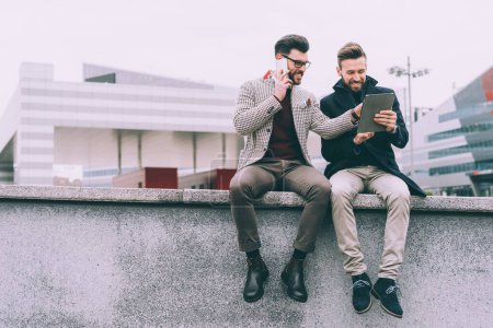 Téléchargez les photos : Deux jeunes hommes d'affaires tablette assis en plein air - en image libre de droit