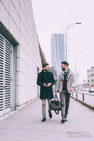 Foto de Dos hombres de negocios jóvenes caminando al aire libre usando el teléfono inteligente - Imagen libre de derechos