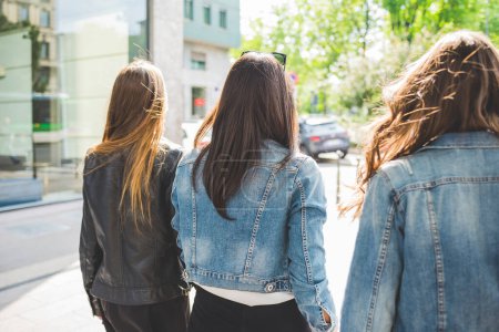 Foto de Vista trasera de tres jóvenes hermosas mujeres caucásicas millennials caminando al aire libre en la ciudad - concepto de amistad - Imagen libre de derechos