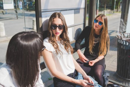 Photo for Three young beautiful women chatting sitting bus station - Royalty Free Image