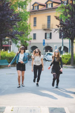 Foto de Tres mujeres jóvenes millennials al aire libre en la ciudad corriendo y saltando divirtiéndose sonriendo - Imagen libre de derechos