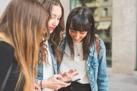 Foto de Tres mujeres jóvenes millennials al aire libre en la ciudad usando el teléfono inteligente - Imagen libre de derechos