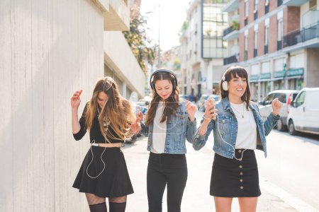 Foto de Tres hermosas jóvenes millennials escuchando música bailando divirtiéndose juntas - Imagen libre de derechos