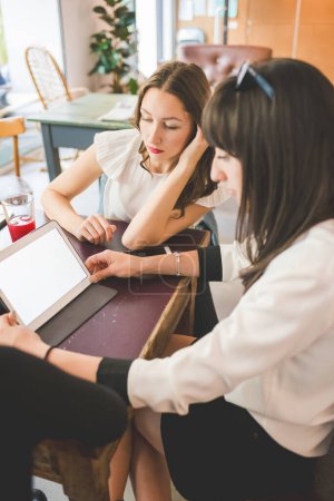 Photo for Three young millennials women indoor using computer discussing - Royalty Free Image