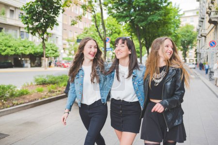 Photo for Three young happy women friends walking outdoors having fun chatting and smiling - Royalty Free Image