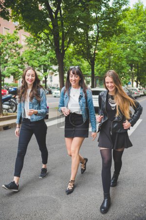 Foto de Tres jóvenes felices amigas caminando al aire libre divirtiéndose charlando y sonriendo - Imagen libre de derechos