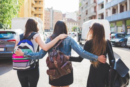 Téléchargez les photos : Arrière vue trois jeunes femmes heureuses amis marchant à l'extérieur étreignant en s'amusant - en image libre de droit