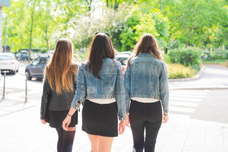 Téléchargez les photos : Vue arrière de trois jeunes femmes milléniales marchant en plein air dans la ville - en image libre de droit