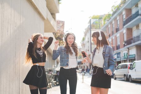 Photo for Three beautiful young women millennials listening music dancing having fun together - Royalty Free Image