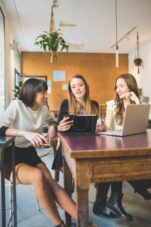 Photo for Three young beautiful caucasian millennials women indoor using computer discussing - Royalty Free Image