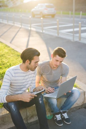 Téléchargez les photos : Deux hommes multiethniques en plein air utilisant PC et tablette - en image libre de droit
