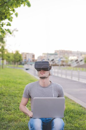 Téléchargez les photos : Jeune homme caucasien utilisant visionneuse 3D et jeux PC en plein air - en image libre de droit