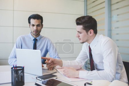 Foto de Dos millennials multiétnicos hombres de negocios usando la computadora trabajando juntos oficina - Imagen libre de derechos