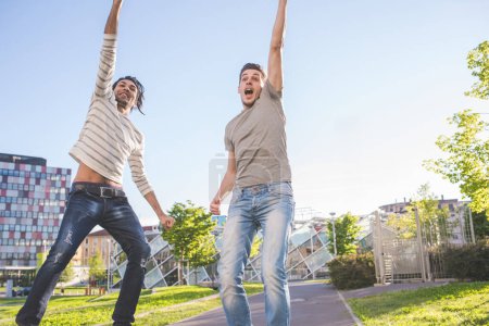 Téléchargez les photos : Deux jeunes hommes multiethniques sautant à l'extérieur célébrant le succès - en image libre de droit