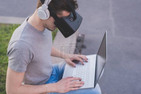 Téléchargez les photos : Jeune homme caucasien utilisant visionneuse 3D et jeux PC en plein air - en image libre de droit