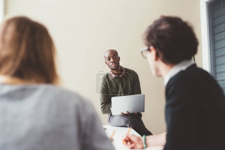 Foto de Tres millennials personas de negocios multiétnicos que se reúnen en interiores utilizando la computadora discutir - Imagen libre de derechos