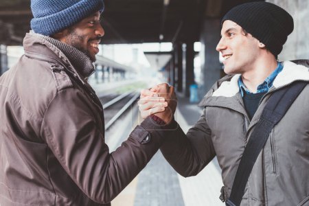 Photo for Two men multiethnic friends shaking hands smiling sayng goodbye railway station - Royalty Free Image