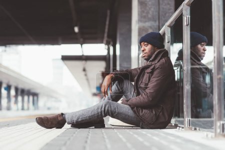 Téléchargez les photos : Jeune homme noir assis gare attendant - en image libre de droit