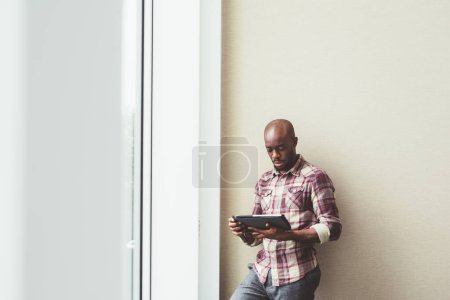 Téléchargez les photos : Jeune homme d'affaires noir posant à l'intérieur en utilisant une tablette - en image libre de droit