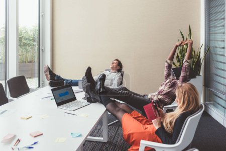Téléchargez les photos : Trois hommes d'affaires se détendre dans le bureau avec les jambes sur la table pendant la pause - en image libre de droit