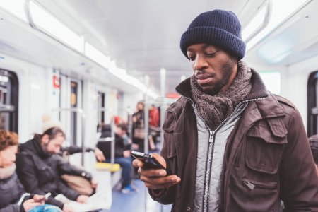 Téléchargez les photos : Jeune homme noir magnifique voyageant sous terre en utilisant un téléphone intelligent - commerce électronique, technologie, concept de voyage - en image libre de droit
