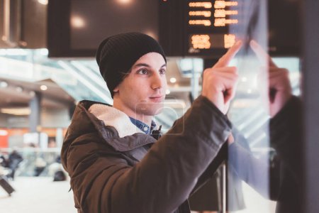 Photo for Young adult caucasian man standing at train station and interacting with touch screen - Royalty Free Image
