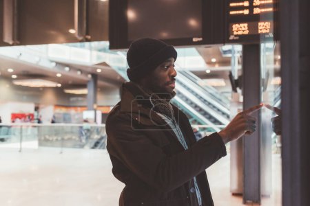 Photo for Young adult black man standing at train station and interacting with touch screen - Royalty Free Image