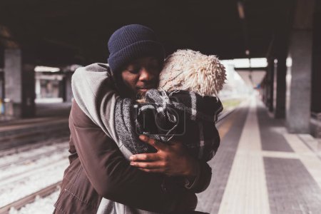 Foto de Pareja multiétnica de pie en la estación de tren y abrazando - Imagen libre de derechos