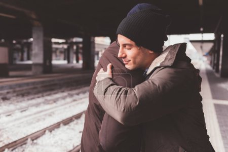 Photo for Multiethnic male friends standing in train station and embracing - Royalty Free Image