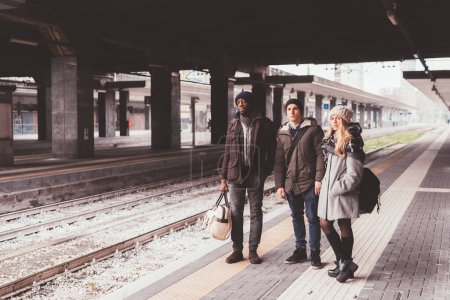 Téléchargez les photos : Trois amis multiethniques plate-forme de train en plein air attente - voyageur, navettage, concept de jour de congé - en image libre de droit