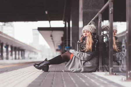 Photo for Young adult woman sitting on the floor and waiting in train station - Royalty Free Image