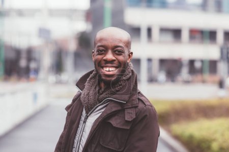 Téléchargez les photos : Portrait de l'homme noir debout en plein air et regardant la caméra souriante - en image libre de droit