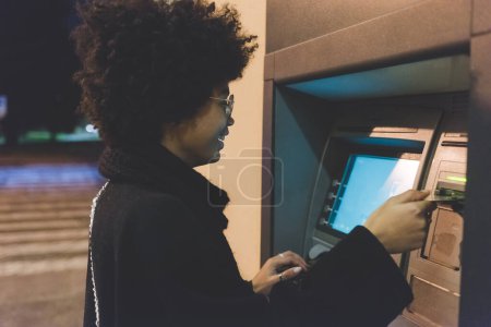 Téléchargez les photos : Jeune femme multiethnique retirant de l'argent de la carte de crédit à guichet automatique - en image libre de droit