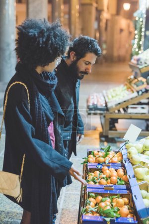 Téléchargez les photos : Jeune couple multiethnique en plein air ville achat de légumes et fruits épicerie - en image libre de droit