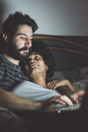 Téléchargez les photos : Jeune couple multiethnique à l'intérieur en utilisant un ordinateur - en image libre de droit