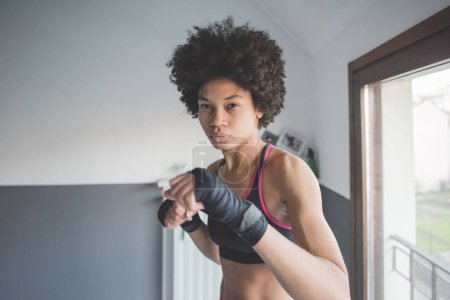 Foto de Mujer joven multiétnico interior entrenamiento boxe en casa - Imagen libre de derechos