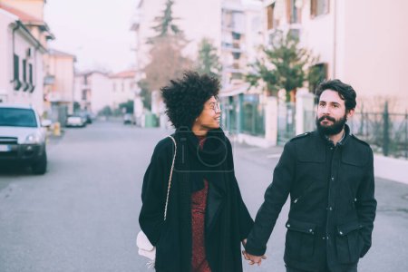 Téléchargez les photos : Jeune couple multiethnique marchant à l'extérieur des rues de la ville au coucher du soleil - en image libre de droit