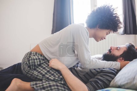 Foto de Joven pareja multiétnica abrazando dormitorio con pijama - Imagen libre de derechos